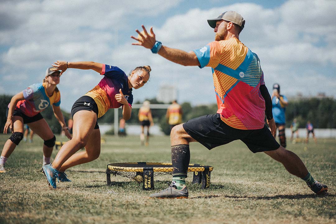 Dva hráči se vrhají a natahují se, aby odpálili míč během zápasu ve Spikeballu na travnatém hřišti