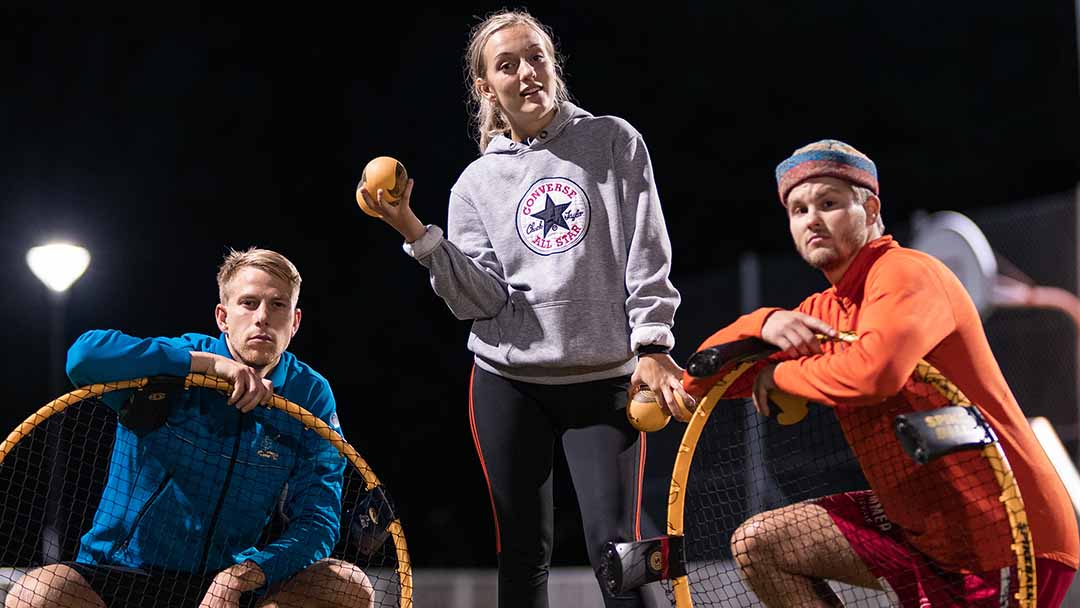 Three players posing with Spikeball nets and balls on an outdoor court at night