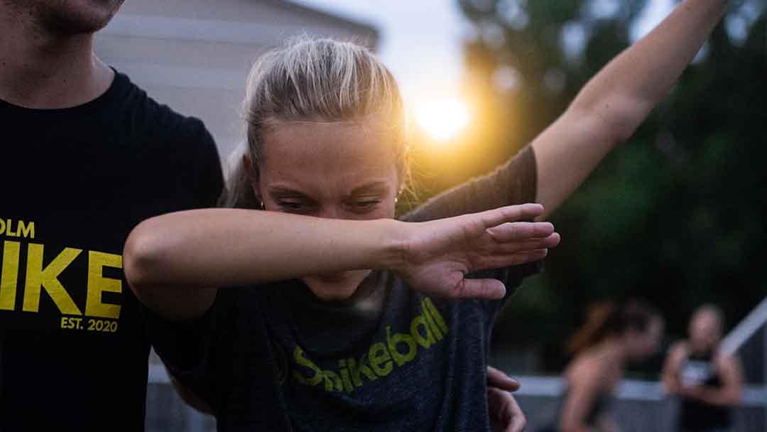 Mujer que se tapa la cara con el brazo mientras celebra con una compañera de equipo durante un partido de Spikeball al aire libre al atardecer