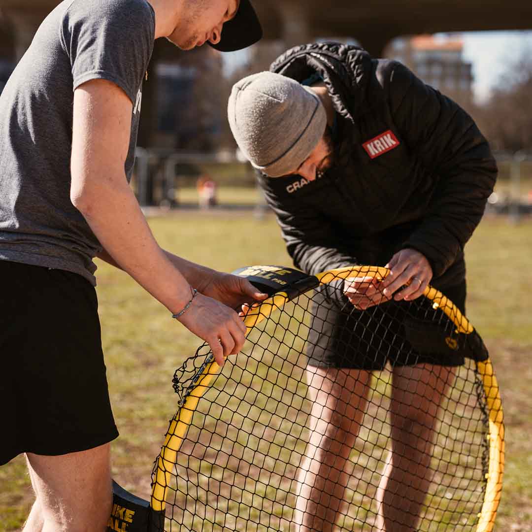 Due giocatori stanno montando una rete di ricambio su un telaio giallo da Spikeball in un campo erboso del parco
