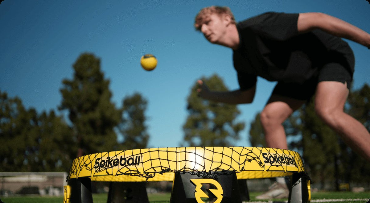 Man playing Spikeball over a yellow net on a grassy field