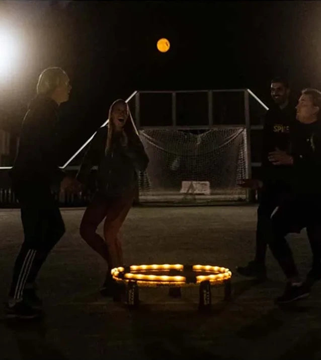 Four Spikeball players using the Spikebrite Kit in a dark court